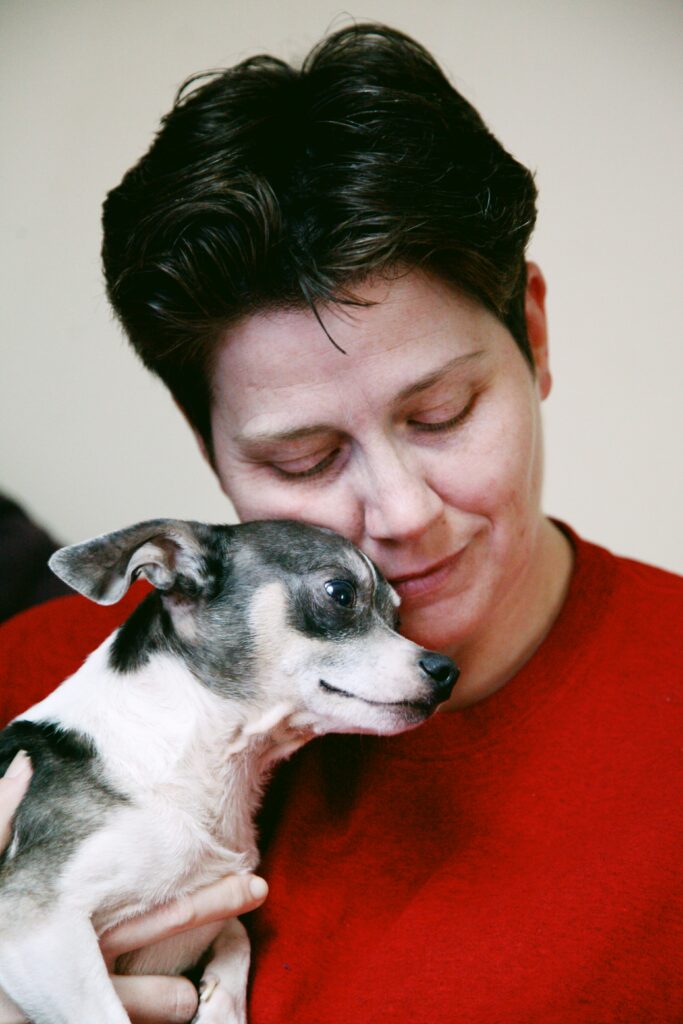 A person holding a small toy dog - older chihuahua close, with the dog resting calmly against them.